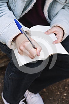 Close-up of a woman`s hands writing in a white notebook in the woods during winter season.