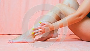 Close-up woman`s legs, girl stroking her legs with a refreshing cream on her legs isolated on a pink background. Skin