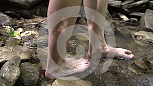 Close up of woman`s legs walking barefoot in mountain river in forest