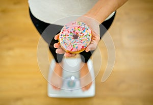 Close up of woman on scale holding delicious donut in obesity and unhealthy food concept