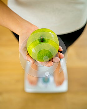 Close up of woman on scale holding fresh green apple in Diet and healthy lifestyle concept