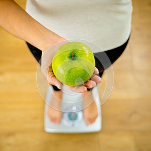 Close up of woman on scale holding fresh green apple in Diet and healthy lifestyle concept