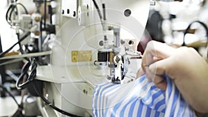Close up of a woman sewing a blue and white shirt at a factory