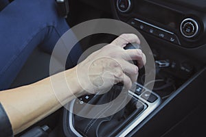 Close up of woman shifting gears on automatic gearbox and driving car. Female hand shifts the hydro sitting in a vehicle. Auto