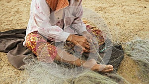 Close-up on a woman sitting down on the riverbank to mend a fishing net by hand 