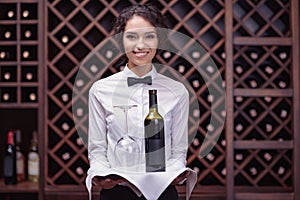 Close-up woman sommelier standing with bottle of wine and glass on tray