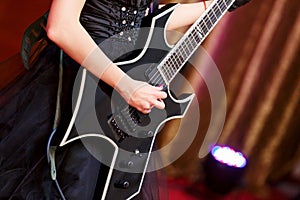 Close-up of a woman on stage playing on electro guitar. The girl rockstar in a black dress