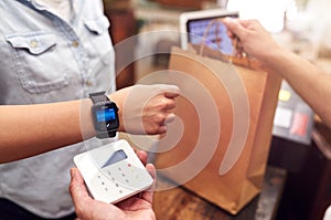 Close Up Of Woman In Store Making Contactless Payment At Sales Desk Holding Smart Watch To Reader