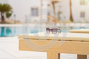 Close-up of woman sunglasses on deck chair near the pool on a bright sunny day. Resort vacation concept of leisure and