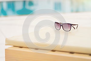 Close-up of woman sunglasses on deck chair near the pool on a bright sunny day. Resort vacation concept of leisure and