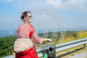 Close up woman with sunglasses stand after ride the bicycle on road on the mountain near row of wind turbines or windmill and she
