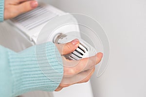 Close-up of a woman in sweater warms her hands over the battery on background of white wall. Macro photo of woman& x27;s