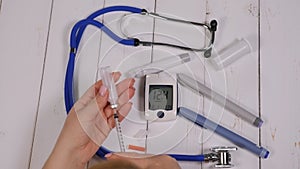 Close-up of a woman taking insulin with a syringe sitting at a wooden table.