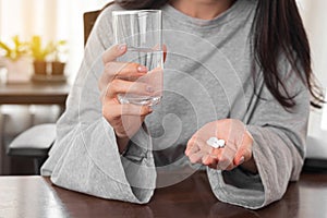 Close up woman taking pill and holding glass of water at home. woman taking medicine after doctor order