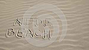 Close up of woman throwing bra at nude beach sign written on sand. Concept of sunbathing naked on the sandy ocean beach.