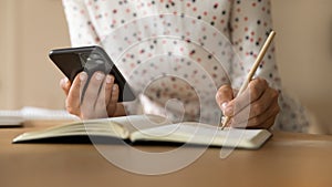Close up of woman use smartphone handwrite making notes
