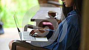 Close-up woman is using a computer laptop while sitting at the wooden chair