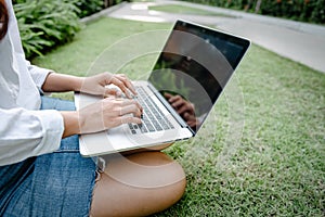 Close-Up of Woman Using Laptop for Business Communication While Sitting on Grass Field. Businesswoman Use Computer Laptop for