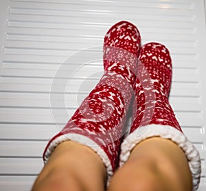 Close-up of a woman warming up her feet on white radiator at home. Central heating concept