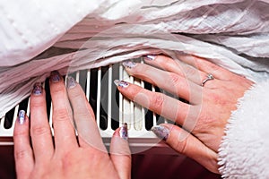 Close-up of a woman warming up her hands on a white radiator at home. Central heating concept