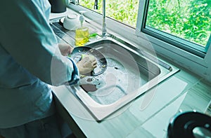 Close-up of a woman washing dishes with dirty food scraps Cleaner in the sink the kitchen counter at home