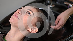 Close-up woman at washing sink in hair parlor with hands of hairdresser turning on water wetting hair. Portrait of