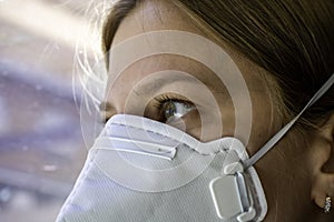 Close up woman wearing a FFP3 face mask looking outside. Disposable respirator protective mouth filter mask