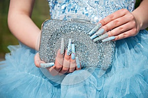 Close-up of a woman wearing a formal light blue dress, her hands with an attractive manicure and sparkling stones, holding a