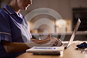 Close Up Of Woman Wearing Medical Scrubs Working Or Studying On Laptop At Home At Night