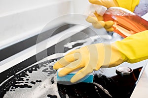 Close Up Of Woman Wearing Rubber Gloves Cleaning Kitchen Hob