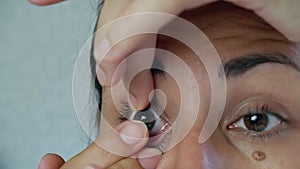 Close-up of a woman wearing soft contact lenses over her eyes against a white background. Myopia.