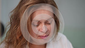 Close-up. A woman in a white bathrobe smiles and laughs while doing a quick morning make-up.