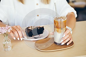 Close-up of woman in white clothes eating in a cafe chocolate cake and drinking ice coffee,