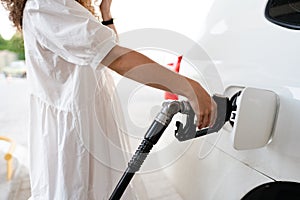 Close up of a woman in white dress refueling her car in a gas station