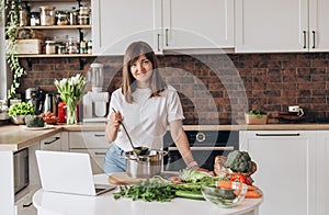 Close up woman in white t-shirt cooking soup with fresh vegetables in kitchen at home. Menu, recipe book banner. Girl