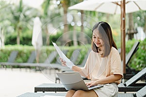 Close-up A woman working at the swimming pool with her laptop computer holding paperwork in her hand. It is imperative for young