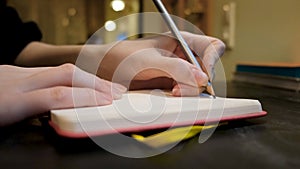 Close-up of woman writing something in notebook in cafe. Concept. Woman writes down something personal or plans day in