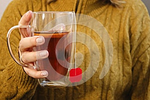 Close up of woman& x27;s hands holding a glass cup with hot tea with lemon and honey