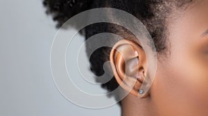 Close-up of a womans ear with stylish silver earring on soft gray background.