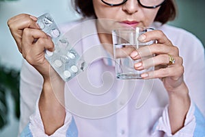 Close-up of womans hand with blister of pills and glass of water