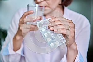Close-up of womans hand with blister of pills and glass of water