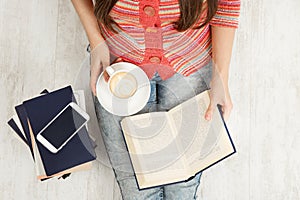 Close up Women Hands Holding Coffee Cup and Reading opened Book. Top view of Woman with Teacup having Break. Sitting Young Girl