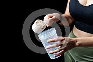 Close up of women with measuring scoop of whey protein and shaker bottle, preparing protein shake