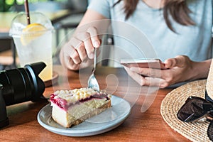 Close up of women`s hands holding mobile phone while eating cake
