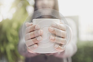 Close up of women`s hands holding white mug. Gray knitted sweater