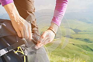 Close-up of women`s hands unfasten the buckle on the camp backpack against the background of the valley in the setting