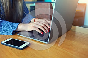 Close up of women`s hands. Woman working on laptop in a cafe. Young woman sitting at a table with a coffee usinglaptop