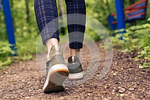 Close-up of women`s legs in green sneakers and pants in a cage go on a forest road. HLS, walk in the open air