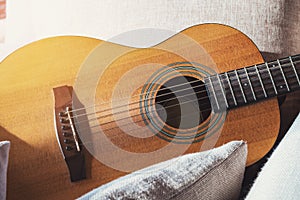 Close-up wooden acoustic guitar on fabric sofa with pillows, vintage tone soft focus