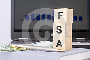 close-up of wooden blocks with the word FSA and banknotes on the background of a laptop